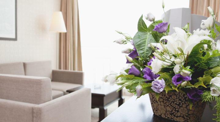 Ein warmes lichtdurchflutetes Hotelzimmer. auf der Komode steht ein Gesteck mit weißen und violettesn Rosen